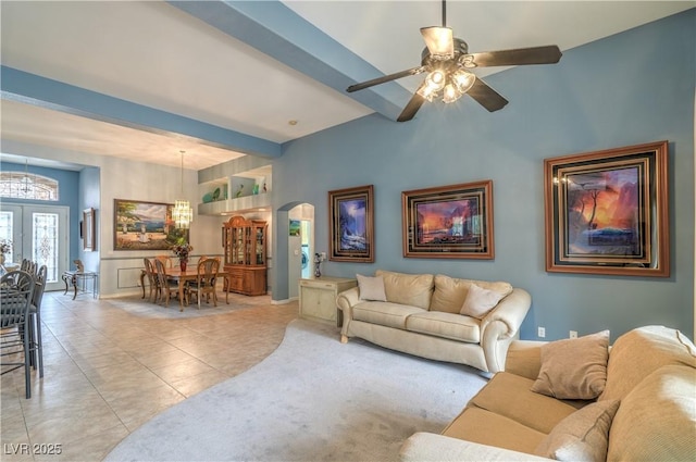 living room with beamed ceiling, light tile patterned floors, ceiling fan with notable chandelier, french doors, and arched walkways