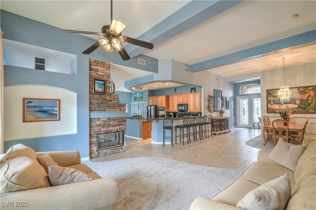 living area with visible vents, beamed ceiling, ceiling fan with notable chandelier, a fireplace, and light tile patterned flooring