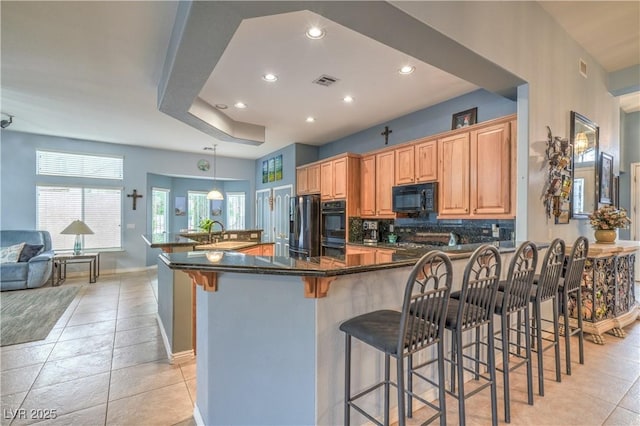 kitchen with visible vents, a breakfast bar, decorative backsplash, light tile patterned flooring, and black appliances