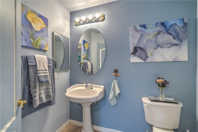 bathroom with baseboards, toilet, and a textured wall