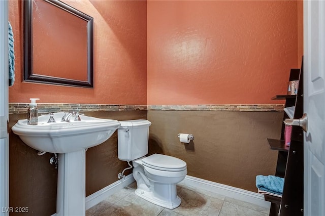 half bathroom with toilet, tile patterned floors, and baseboards