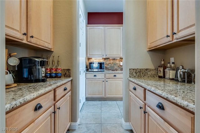 kitchen featuring stainless steel microwave, light stone countertops, tasteful backsplash, and light brown cabinets