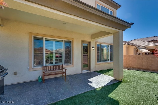 view of exterior entry featuring fence, stucco siding, a patio, and a yard