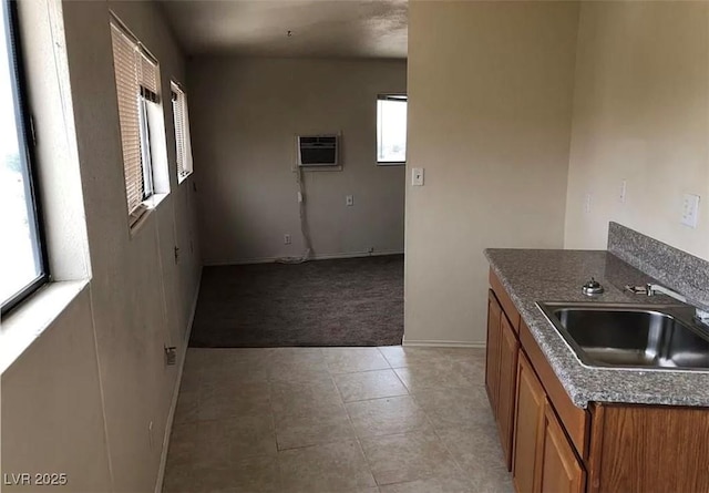 kitchen with a wall unit AC, brown cabinetry, light carpet, a sink, and baseboards