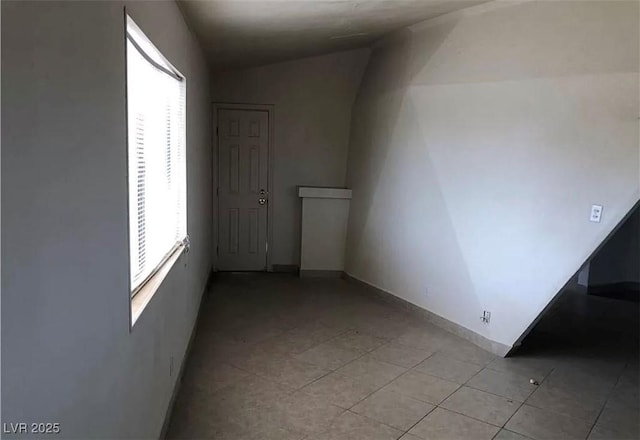 empty room featuring lofted ceiling, plenty of natural light, light tile patterned flooring, and baseboards