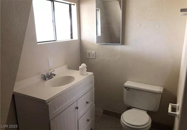 bathroom with a textured wall, vanity, toilet, and baseboards