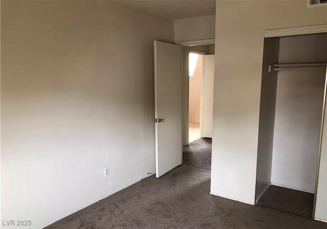 unfurnished bedroom with dark colored carpet, a closet, and visible vents