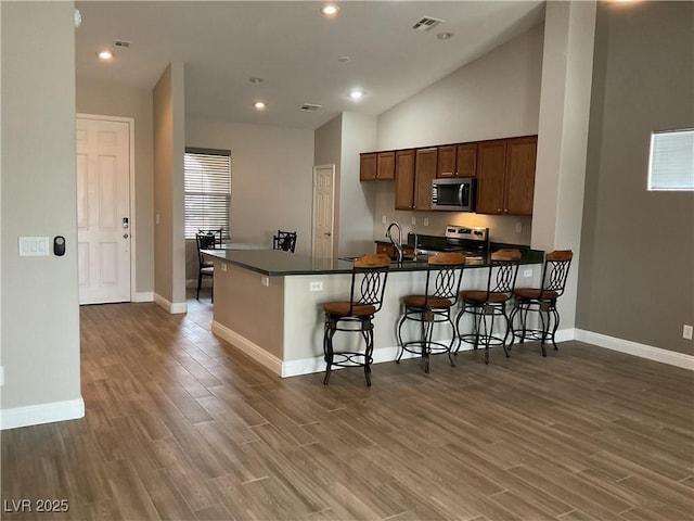 kitchen featuring visible vents, dark countertops, a breakfast bar, wood finished floors, and stainless steel appliances