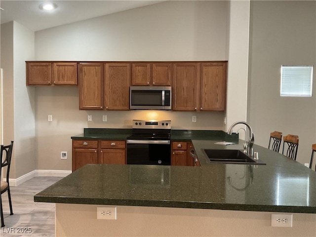 kitchen featuring a peninsula, a sink, appliances with stainless steel finishes, light wood-type flooring, and brown cabinets