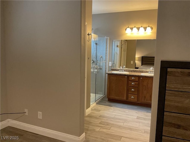 ensuite bathroom featuring a stall shower, connected bathroom, vanity, wood finished floors, and baseboards