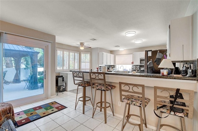 kitchen with a peninsula, white cabinets, stainless steel microwave, dark countertops, and a kitchen bar