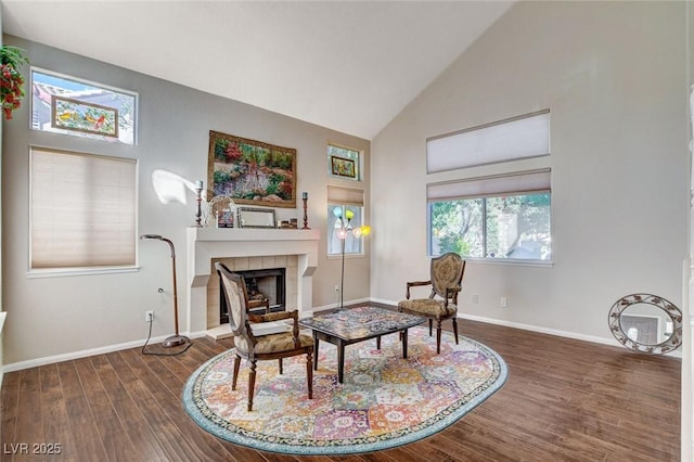 living area featuring dark wood-type flooring, a tile fireplace, high vaulted ceiling, and baseboards