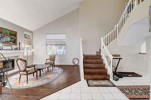 entrance foyer featuring high vaulted ceiling, tile patterned flooring, a tiled fireplace, and stairs