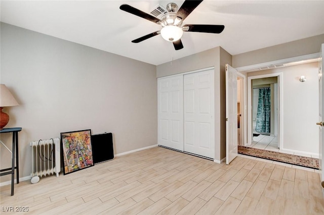 unfurnished bedroom featuring baseboards, radiator, ceiling fan, wood finished floors, and a closet