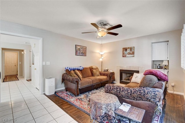 living area featuring a ceiling fan, baseboards, a fireplace, and light wood finished floors