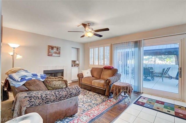 living area featuring ceiling fan, a tile fireplace, and tile patterned flooring