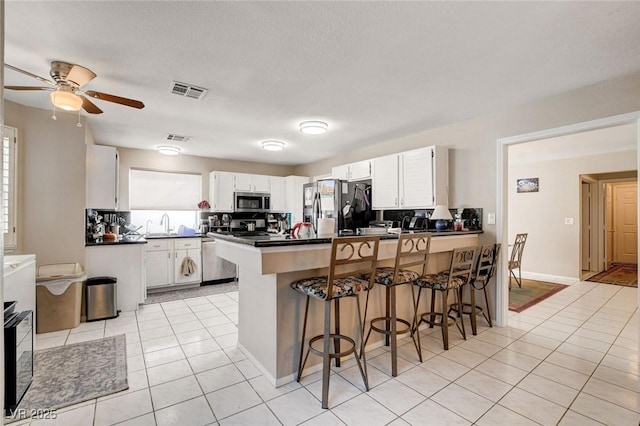 kitchen featuring a peninsula, dark countertops, appliances with stainless steel finishes, and light tile patterned flooring