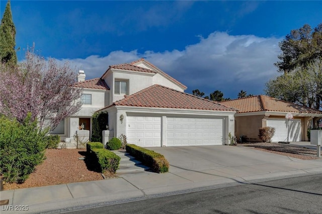 mediterranean / spanish home with an attached garage, a tile roof, driveway, stucco siding, and a chimney