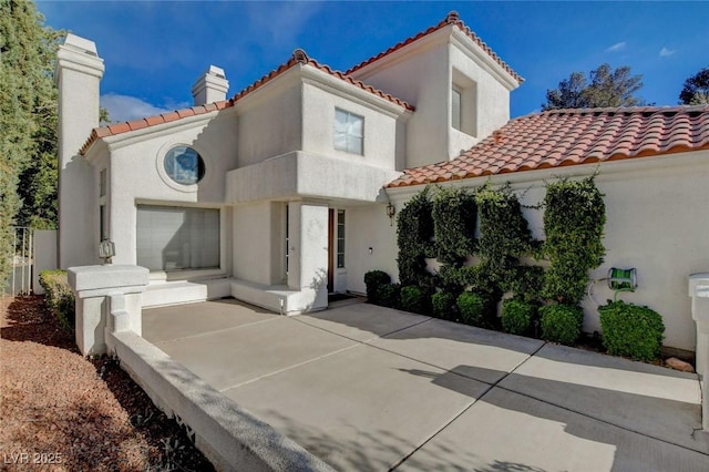 mediterranean / spanish home featuring a tile roof, a chimney, and stucco siding