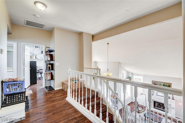 hall with baseboards, visible vents, wood finished floors, an upstairs landing, and a chandelier