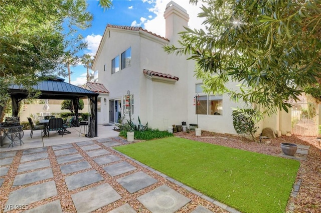 rear view of property with a tile roof, a yard, a gazebo, a patio area, and stucco siding