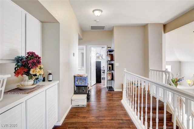 corridor with dark wood-style floors, baseboards, visible vents, and an upstairs landing