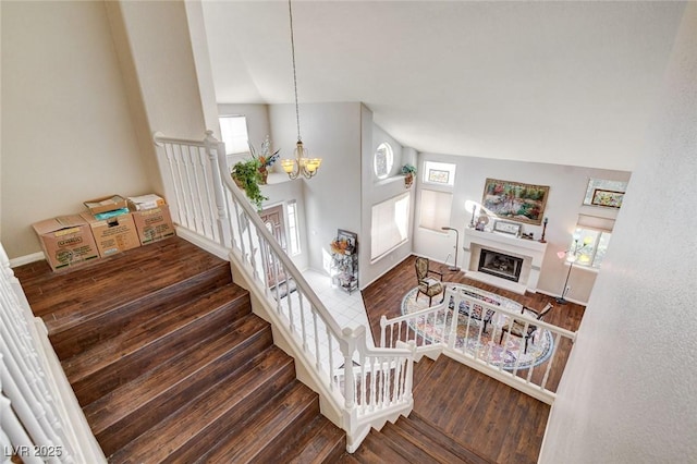 stairs with a healthy amount of sunlight, a fireplace, an inviting chandelier, and wood finished floors