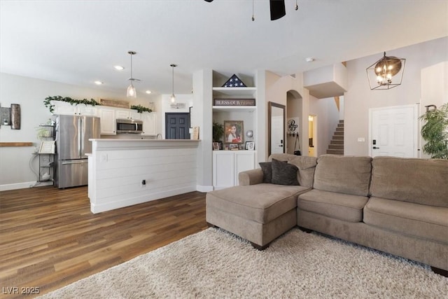 living area featuring arched walkways, a ceiling fan, baseboards, stairway, and dark wood-style floors