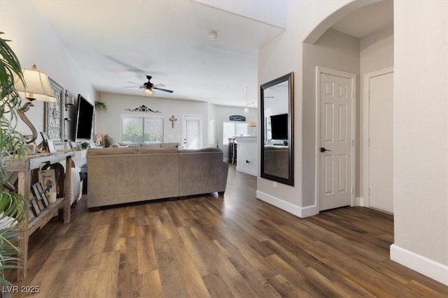 living room featuring arched walkways, dark wood-type flooring, a ceiling fan, and baseboards