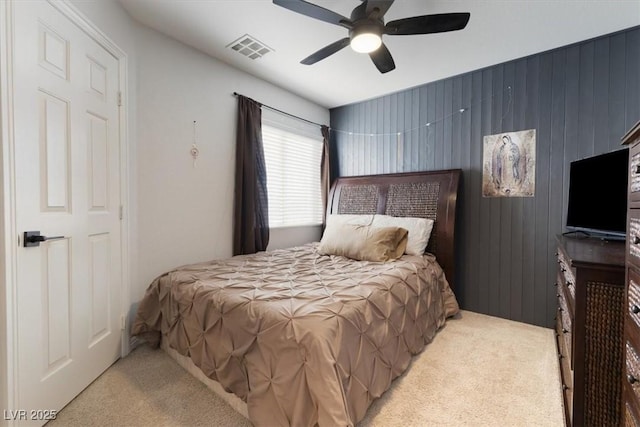 bedroom with light carpet, ceiling fan, wood walls, and visible vents