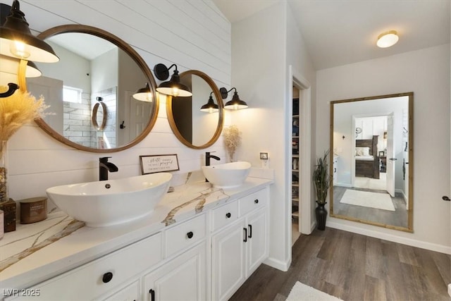 ensuite bathroom with double vanity, wood finished floors, a sink, and connected bathroom