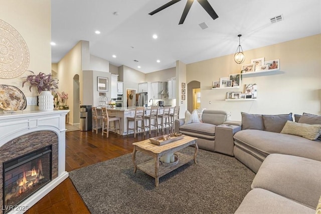 living room with dark wood-type flooring, arched walkways, visible vents, and a glass covered fireplace