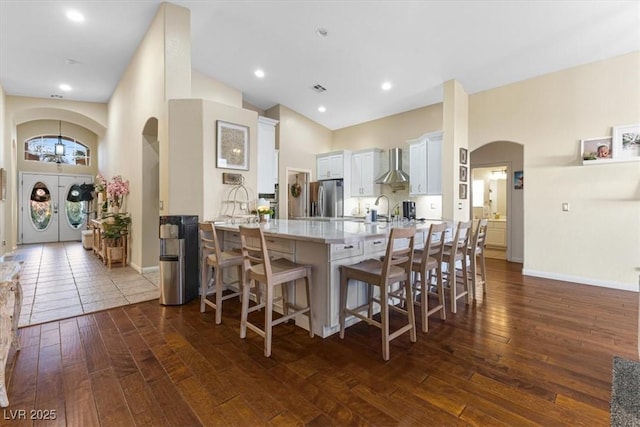 kitchen featuring arched walkways, a peninsula, dark wood-style flooring, wall chimney exhaust hood, and stainless steel fridge