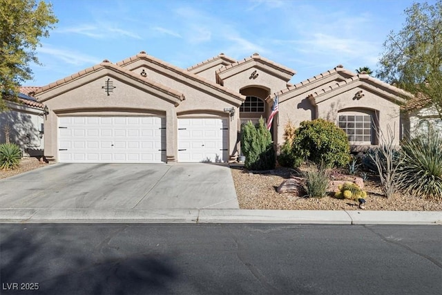 mediterranean / spanish home with a garage, driveway, a tiled roof, and stucco siding