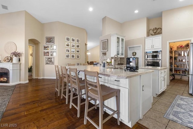 kitchen with a warm lit fireplace, arched walkways, white cabinets, a large island, and a breakfast bar area