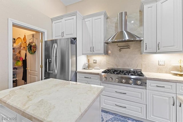 kitchen featuring light stone countertops, white cabinets, appliances with stainless steel finishes, wall chimney range hood, and decorative backsplash