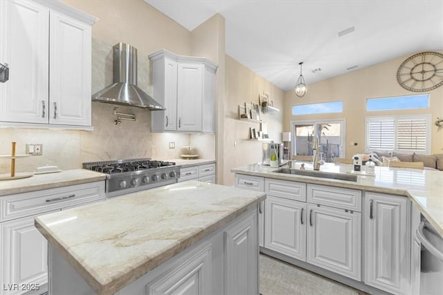 kitchen featuring a center island, stainless steel appliances, wall chimney range hood, white cabinetry, and a sink