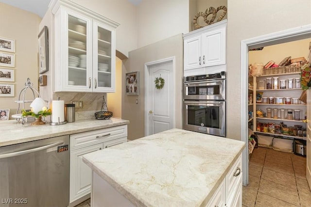 kitchen with tasteful backsplash, appliances with stainless steel finishes, glass insert cabinets, white cabinetry, and light stone countertops