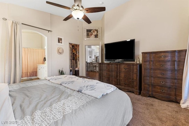 bedroom with arched walkways, ceiling fan, ensuite bathroom, carpet flooring, and a towering ceiling