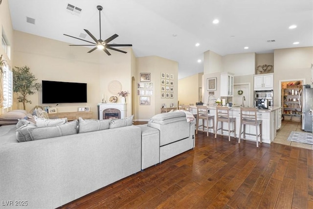 living area with a ceiling fan, visible vents, a fireplace, and hardwood / wood-style floors