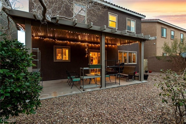 back of house at dusk featuring a patio area, fence, a pergola, and stucco siding