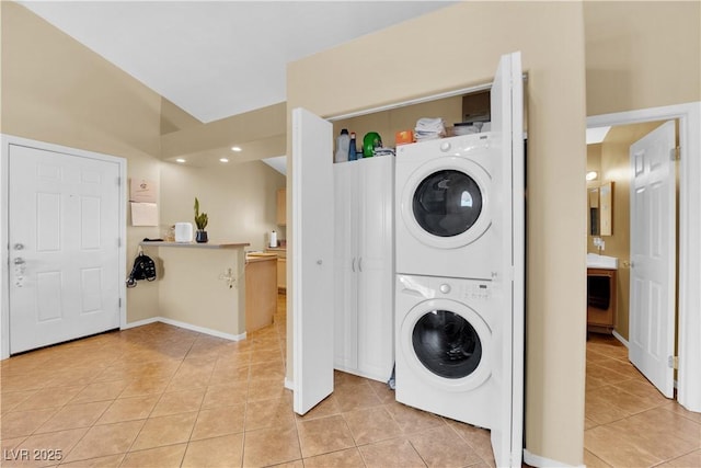 clothes washing area featuring light tile patterned floors, stacked washer and dryer, and laundry area