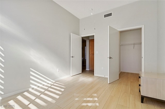 unfurnished bedroom with a towering ceiling, baseboards, visible vents, light wood-style floors, and a closet