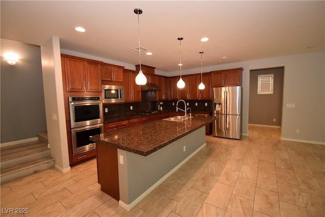 kitchen featuring recessed lighting, stainless steel appliances, a sink, backsplash, and an island with sink