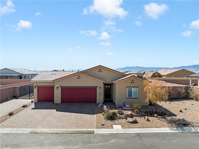 view of front of home featuring fence, stucco siding, decorative driveway, a garage, and a mountain view