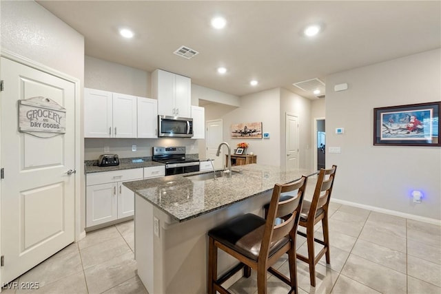 kitchen with visible vents, stone counters, a breakfast bar, a sink, and stainless steel appliances