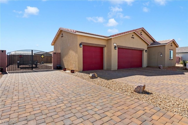 view of front facade with stucco siding, an attached garage, decorative driveway, and a gate