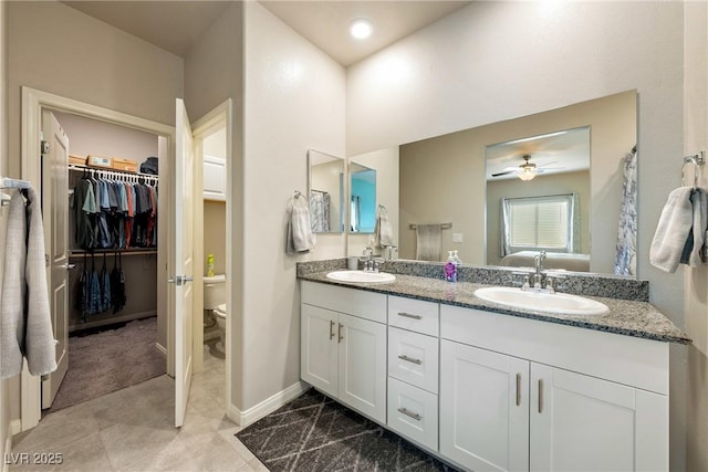 bathroom featuring a walk in closet, double vanity, toilet, and a sink