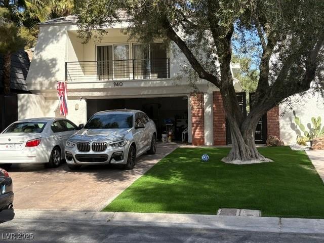 view of front of property featuring driveway, a balcony, stucco siding, an attached garage, and a front yard