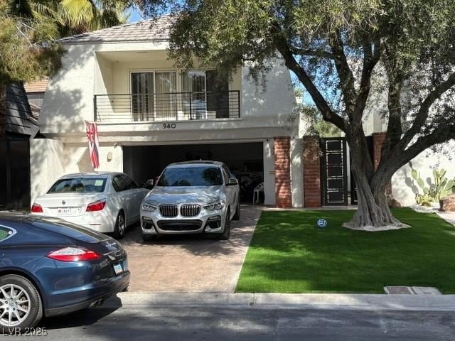 view of front of property with driveway, a garage, a balcony, stucco siding, and a front yard